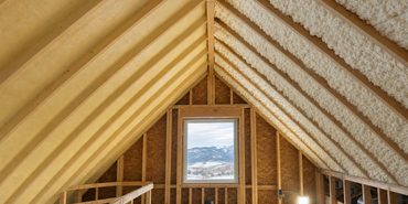 Attic rafters in a Northern Colorado home with dense yellow closed-cell spray foam on one side of the roof deck and thick white open-cell spray foam on the other